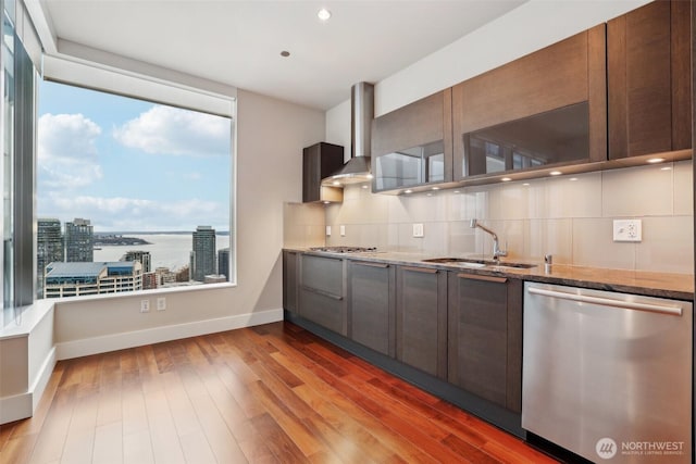 kitchen with stone counters, stainless steel appliances, backsplash, a sink, and wall chimney range hood