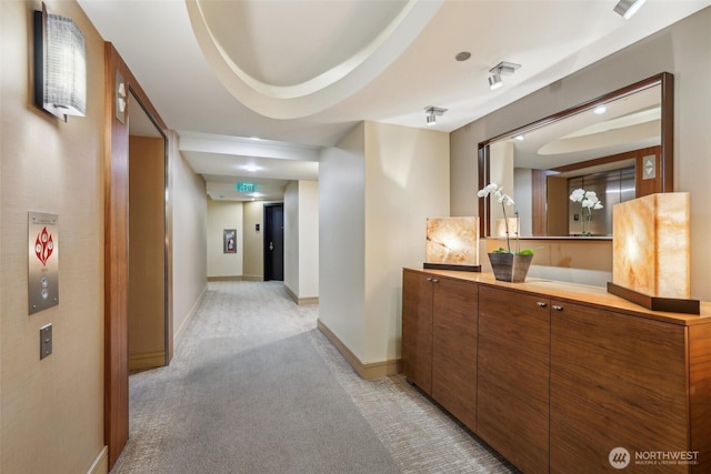 hall with a tray ceiling, light carpet, and baseboards