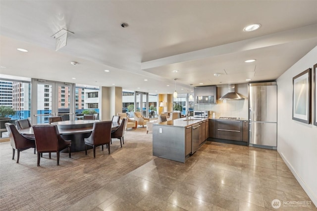 kitchen featuring wall chimney exhaust hood, modern cabinets, open floor plan, a peninsula, and recessed lighting