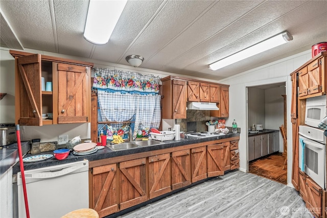 kitchen with under cabinet range hood, white appliances, brown cabinets, and light wood-style flooring