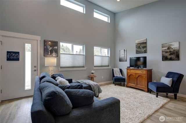 living area with a towering ceiling, light wood-style floors, and baseboards