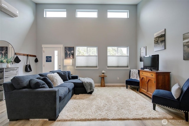 living area with a healthy amount of sunlight, a towering ceiling, baseboards, and a wall mounted AC