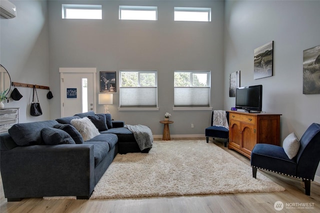 living room featuring a wall mounted air conditioner, a healthy amount of sunlight, a towering ceiling, and wood finished floors