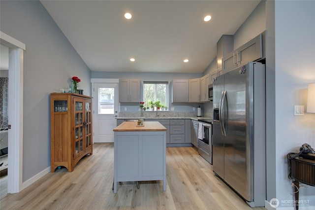 kitchen featuring a center island, stainless steel appliances, gray cabinets, light wood-style floors, and butcher block countertops