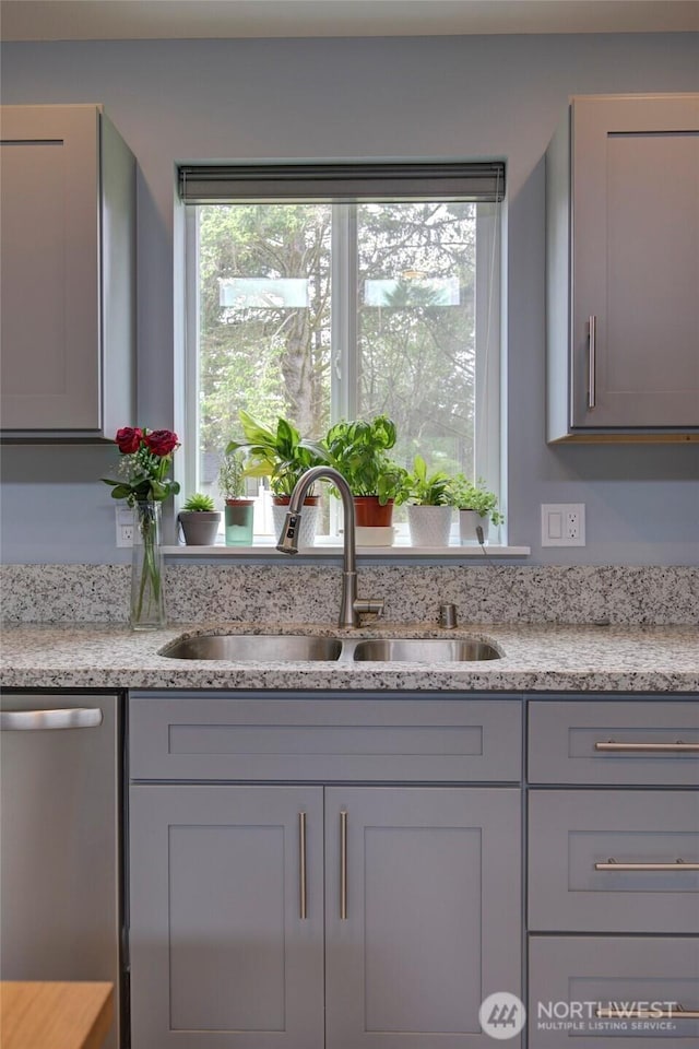 kitchen with a sink, light stone countertops, stainless steel dishwasher, and gray cabinetry