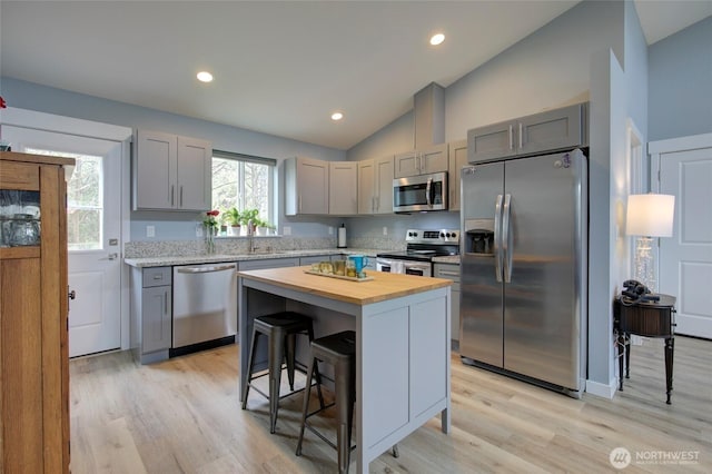 kitchen featuring lofted ceiling, butcher block counters, a breakfast bar area, gray cabinets, and stainless steel appliances