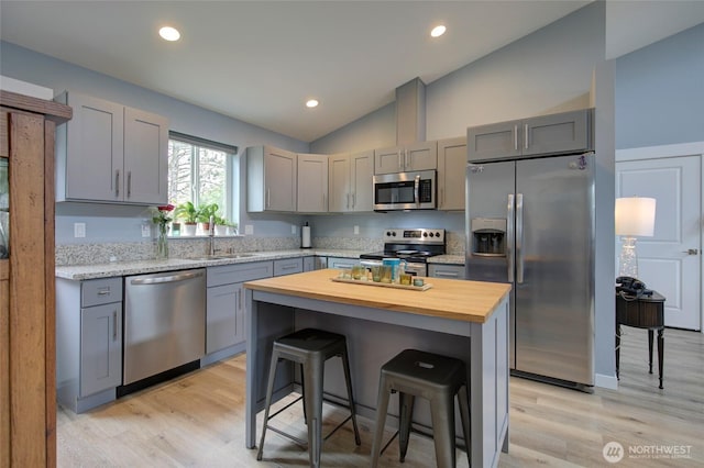 kitchen featuring lofted ceiling, gray cabinetry, stainless steel appliances, butcher block countertops, and a breakfast bar