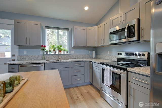 kitchen featuring appliances with stainless steel finishes, lofted ceiling, gray cabinets, and a sink