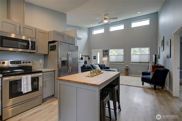 kitchen with stainless steel appliances, gray cabinets, open floor plan, butcher block countertops, and a kitchen breakfast bar