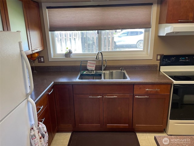 kitchen featuring under cabinet range hood, a sink, freestanding refrigerator, electric range oven, and dark countertops