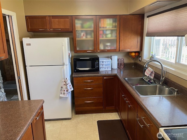 kitchen with white appliances, dark countertops, a sink, and glass insert cabinets