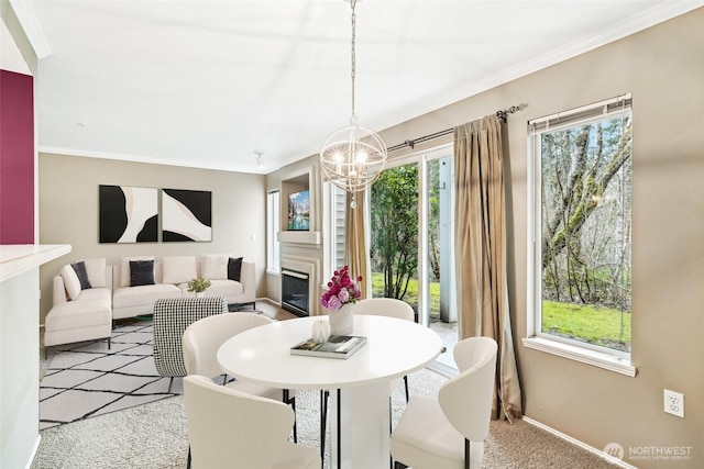 carpeted dining area with baseboards, a chandelier, ornamental molding, and a glass covered fireplace