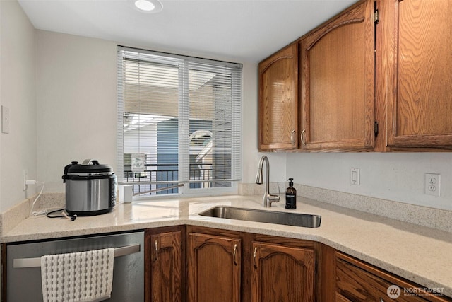 kitchen with a sink, brown cabinetry, light countertops, and dishwasher