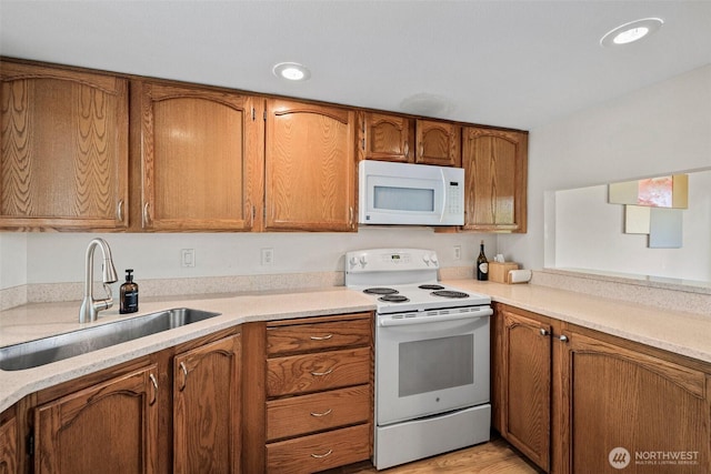 kitchen with white appliances, brown cabinetry, a sink, and light countertops