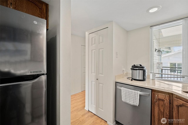 kitchen featuring stainless steel appliances, brown cabinetry, and light wood finished floors