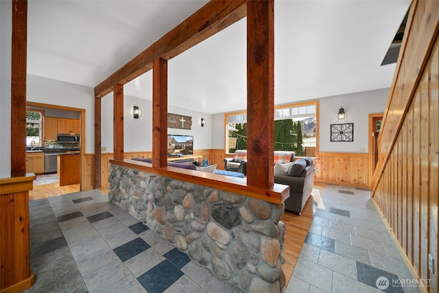 kitchen featuring beam ceiling, stone tile flooring, stainless steel appliances, wood walls, and wainscoting