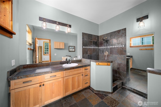 full bath featuring stone tile floors, a walk in shower, and vanity