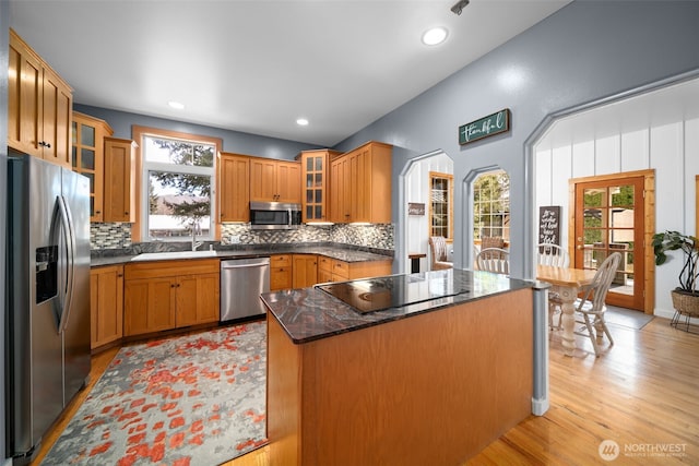 kitchen with decorative backsplash, light wood-style flooring, brown cabinetry, stainless steel appliances, and a sink