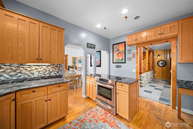 kitchen with arched walkways, tasteful backsplash, stainless steel electric range, and light wood finished floors