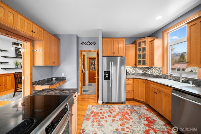 kitchen featuring backsplash, glass insert cabinets, appliances with stainless steel finishes, light wood-style floors, and a sink