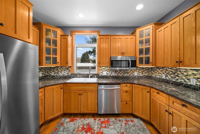 kitchen with a sink, stainless steel appliances, glass insert cabinets, light wood-style floors, and tasteful backsplash