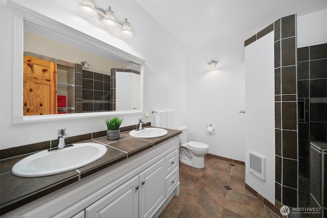 bathroom with heating unit, double vanity, toilet, and a sink