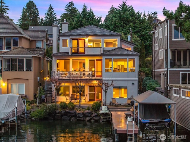 back of property at dusk with a chimney, stairway, a tiled roof, a water view, and stucco siding