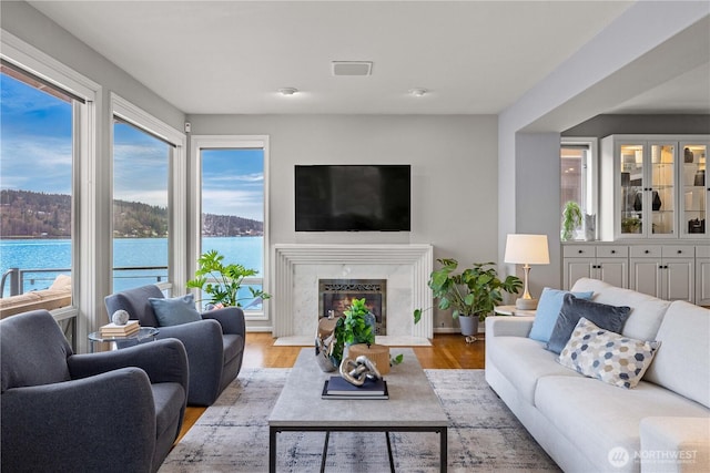 living room featuring a high end fireplace, visible vents, baseboards, and wood finished floors