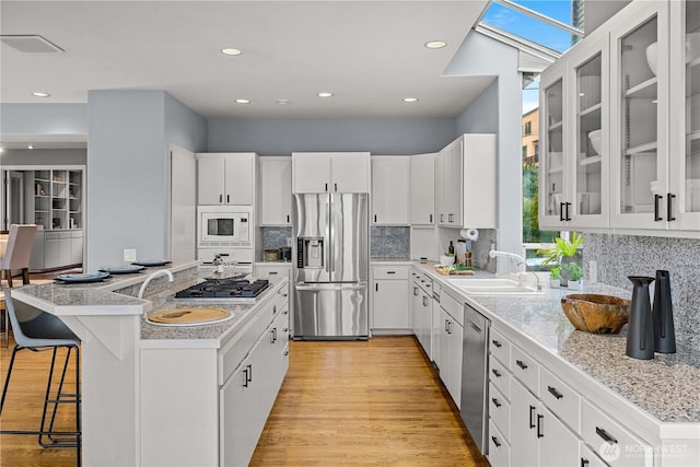 kitchen featuring a breakfast bar, a sink, light wood-style floors, light countertops, and appliances with stainless steel finishes