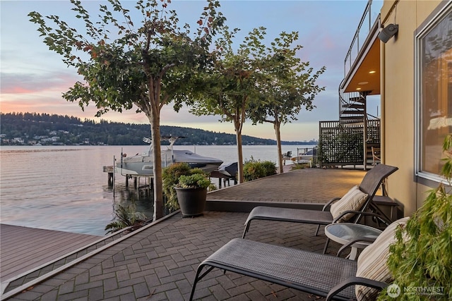 patio terrace at dusk with stairway, a water view, and a boat dock