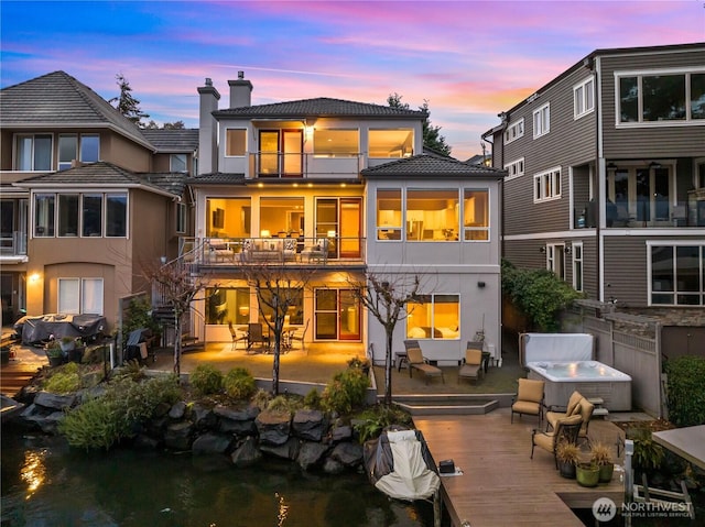 back of house with a patio, a balcony, stucco siding, a chimney, and a hot tub