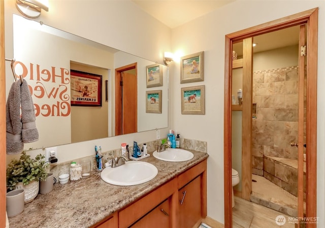 bathroom featuring a tile shower, double vanity, a sink, and toilet