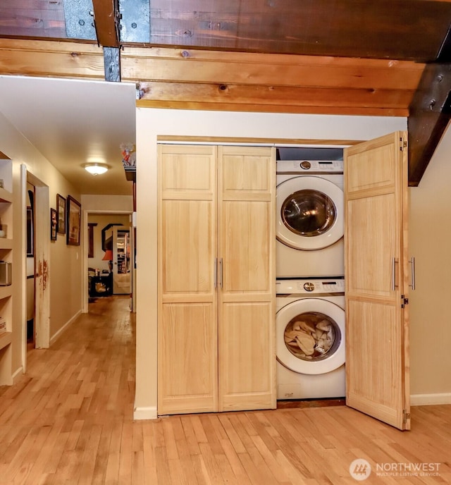 laundry area with stacked washer / dryer, laundry area, baseboards, and light wood finished floors