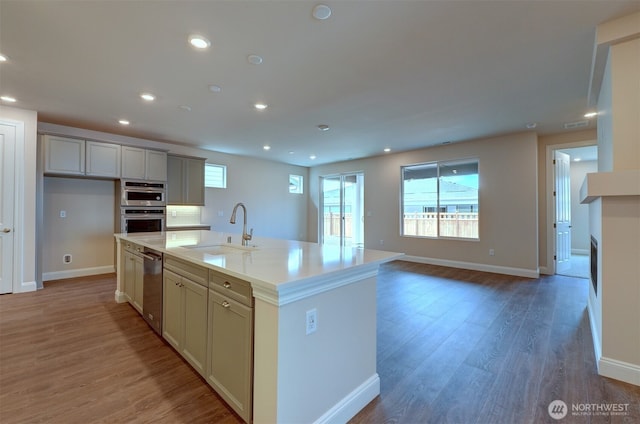 kitchen featuring a center island with sink, recessed lighting, double oven, a sink, and light wood-type flooring