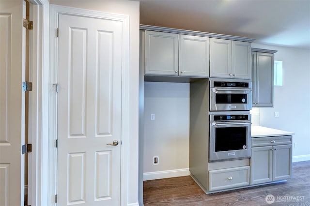 kitchen with double oven, dark wood-style flooring, baseboards, light countertops, and gray cabinets