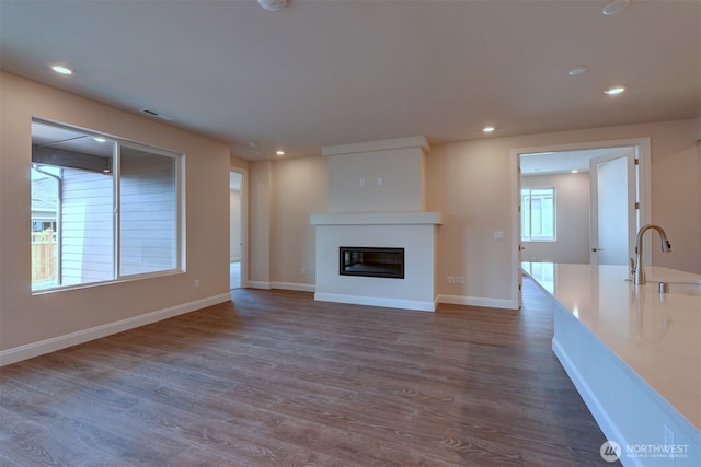 unfurnished living room featuring recessed lighting, dark wood-type flooring, a sink, baseboards, and a glass covered fireplace