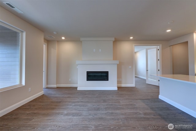 unfurnished living room featuring a glass covered fireplace, dark wood-style flooring, visible vents, and recessed lighting