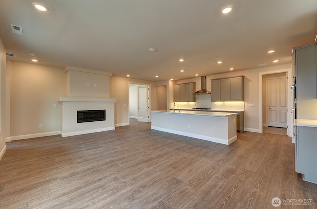 kitchen with light wood finished floors, wall chimney range hood, backsplash, and gray cabinets