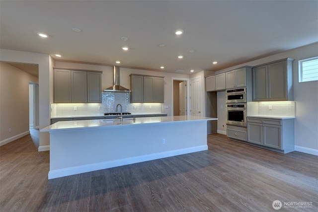 kitchen featuring dark wood-style floors, wall chimney exhaust hood, a center island with sink, and gray cabinets