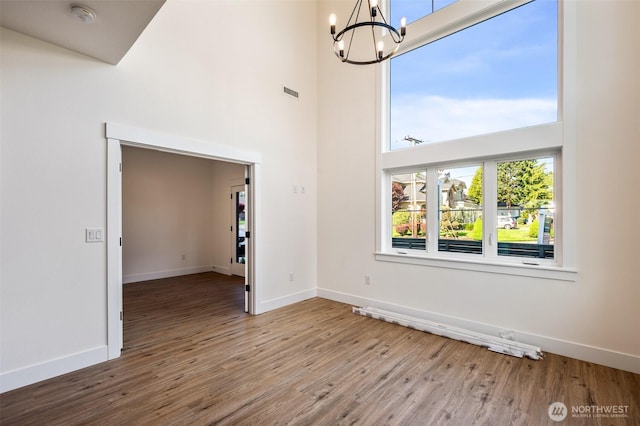 unfurnished room featuring wood finished floors, a towering ceiling, baseboards, and an inviting chandelier