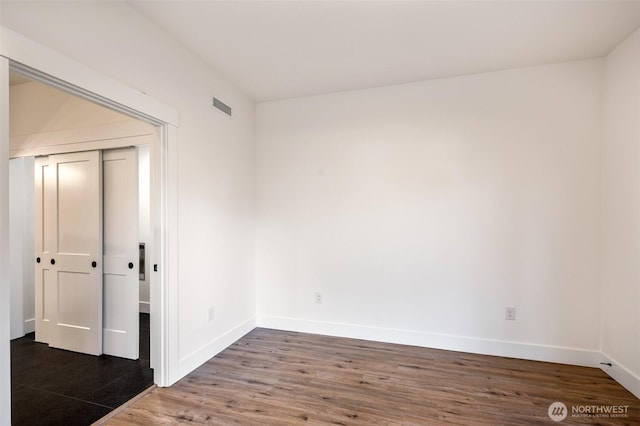 spare room featuring wood finished floors, visible vents, and baseboards