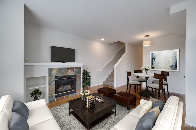 living room with a tile fireplace, recessed lighting, wood finished floors, baseboards, and stairway