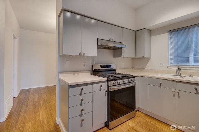 kitchen featuring light countertops, stainless steel gas stove, a sink, light wood-type flooring, and under cabinet range hood