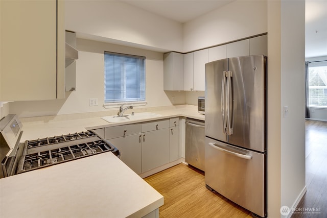 kitchen featuring a sink, baseboards, light countertops, appliances with stainless steel finishes, and light wood finished floors