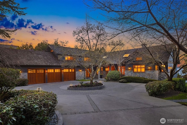 view of front of property featuring a garage, stone siding, and curved driveway