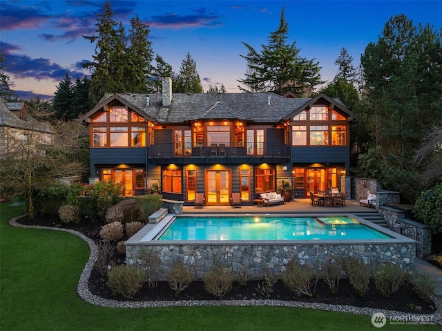 rear view of house featuring a chimney, a yard, a balcony, a patio area, and an outdoor pool