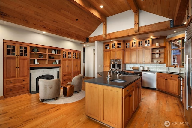 kitchen featuring dark countertops, open shelves, a tiled fireplace, stainless steel appliances, and a sink