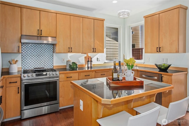 kitchen with dark wood-style floors, a breakfast bar, a kitchen island, under cabinet range hood, and stainless steel gas range oven