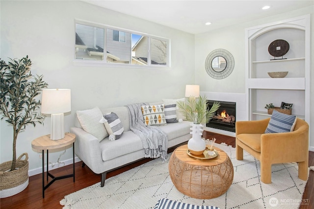 living room with baseboards, built in features, wood finished floors, a lit fireplace, and recessed lighting