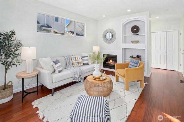 living area with built in features, a glass covered fireplace, recessed lighting, and wood finished floors